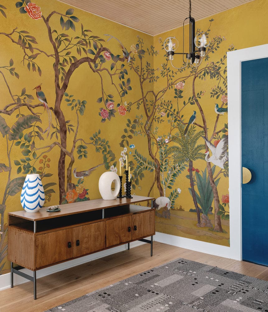 Golden Chinoiserie Garden Mural Wallpaper, vibrant birds, flowers, and wooden sideboard in stylish room.