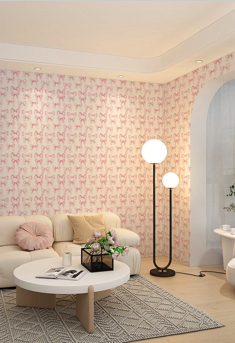 Elegant pink bow pattern wallpaper in cosy living room with cream sofa, wooden flooring, modern lamps.