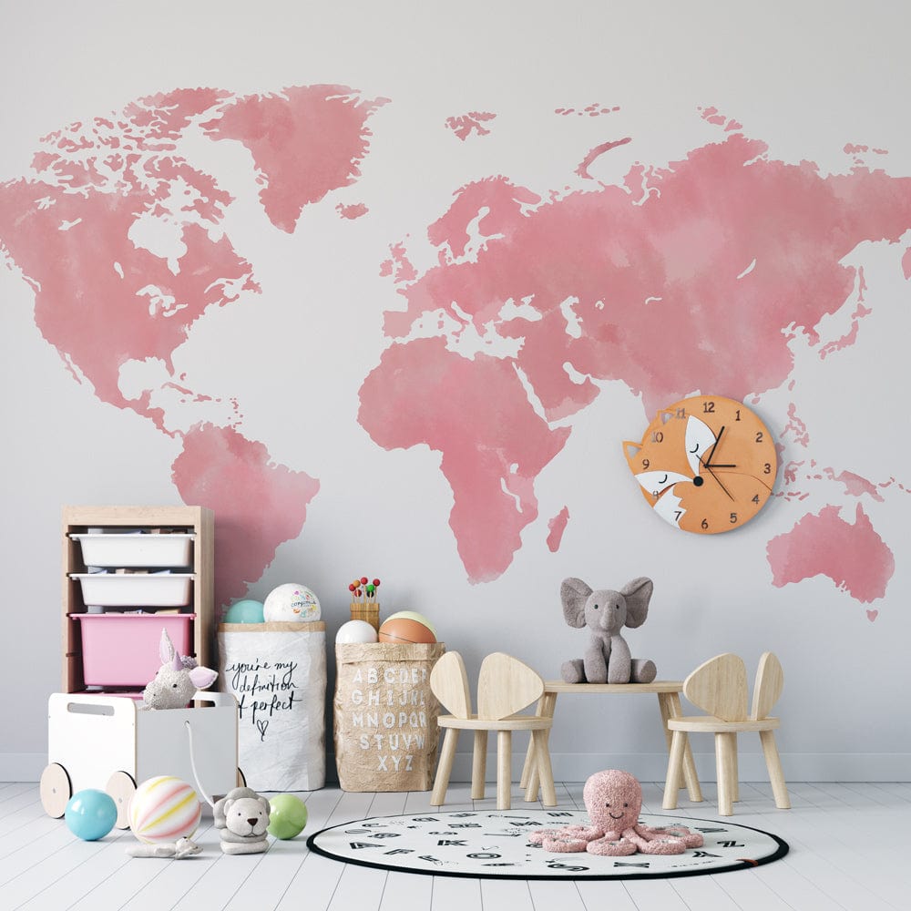 Blush pink watercolour world map mural wallpaper, modern playroom setting, light wood flooring, wooden chairs.