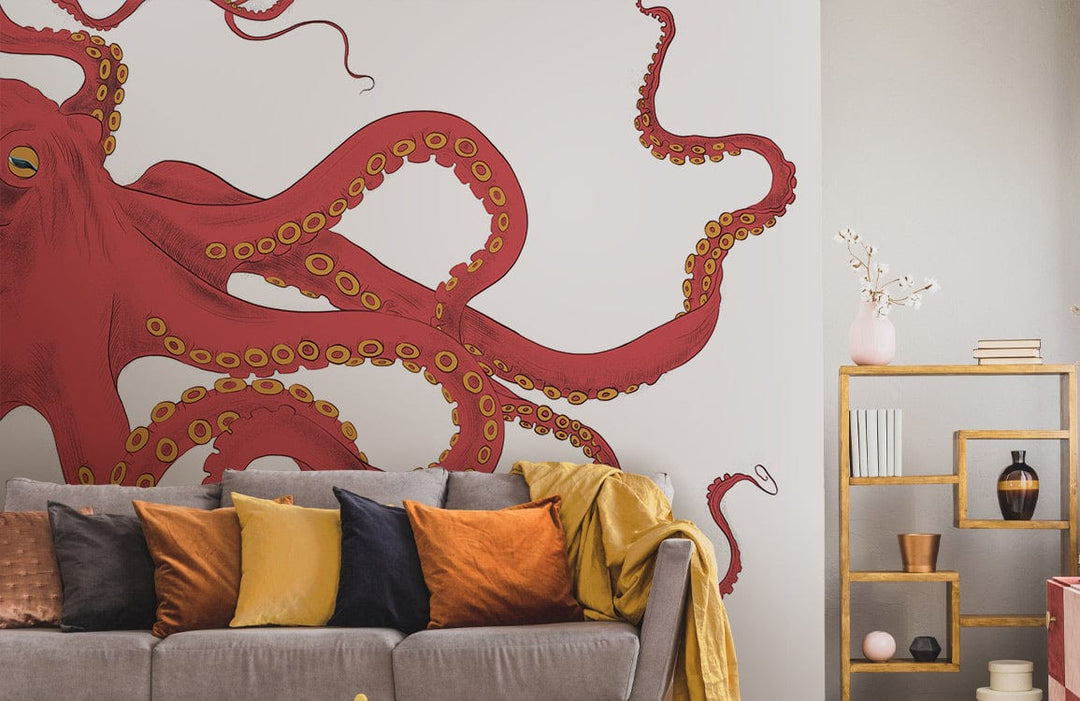 Vibrant red octopus mural wallpaper in living room with grey sofa, colourful cushions, and gold shelves.