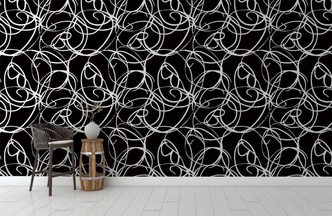 Intricate black and white Art Nouveau wallpaper, wooden flooring, wicker chair, vase on side table.