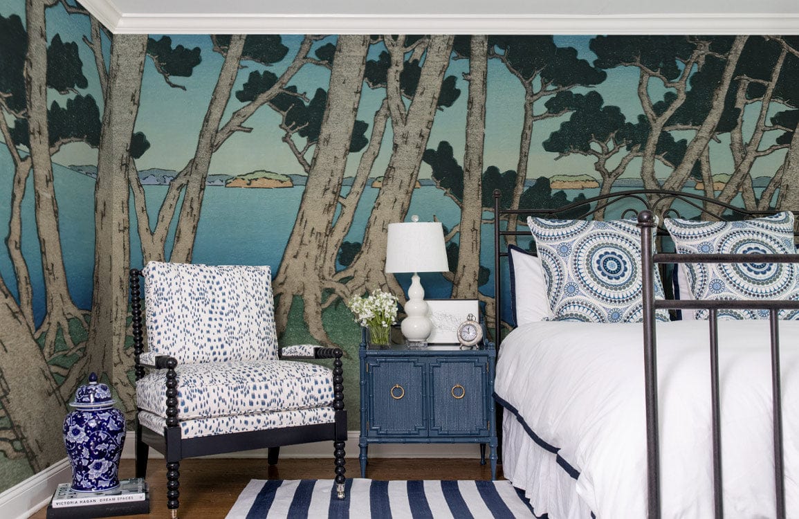 Tranquil Coastal Forest Scene mural wallpaper in bedroom with patterned chair, blue bedside table, striped rug.