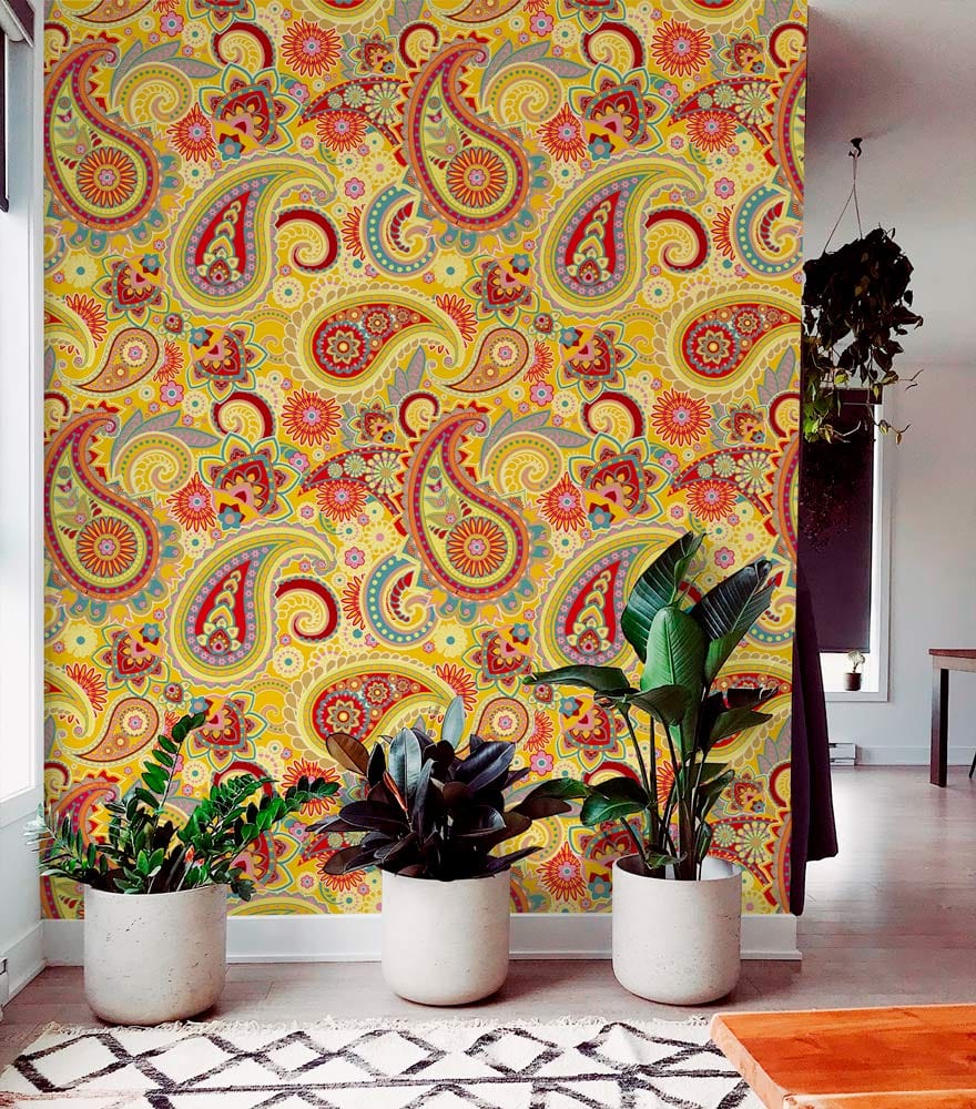 Vibrant multicoloured paisley wallpaper in room with plants, wooden flooring, and patterned rug.
