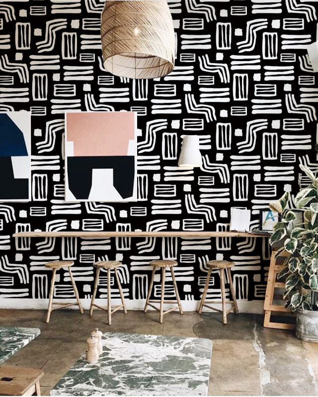 Monochrome geometric tribal wallpaper, wooden stools, contemporary pendant lights, art prints, concrete flooring, indoor plant.