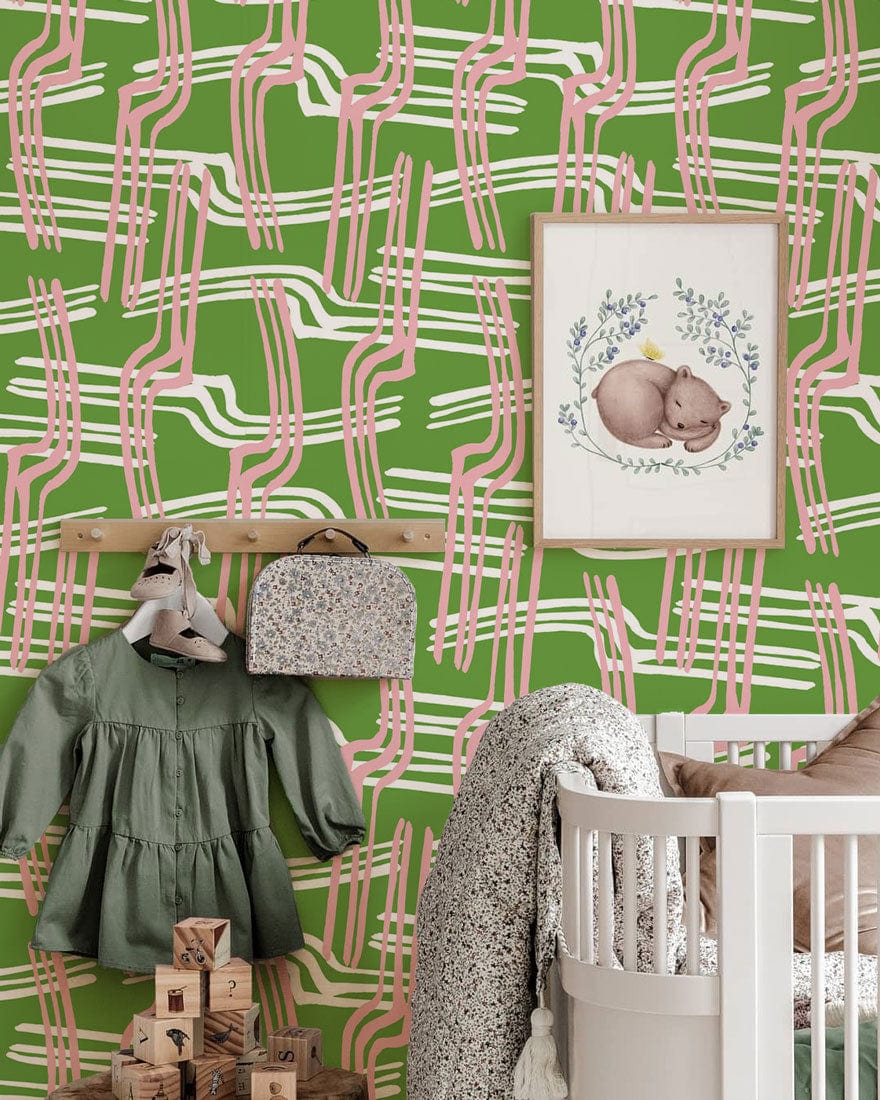 Geometric pink and green abstract patterned wallpaper in nursery with white cot, green dress, artwork.
