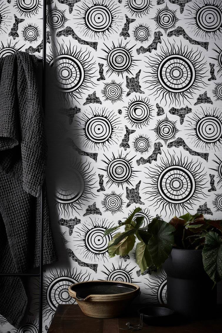 Monochrome Sunburst Mandala Wallpaper, black white retro elegance, textured wall, patterned fabric draped nearby.