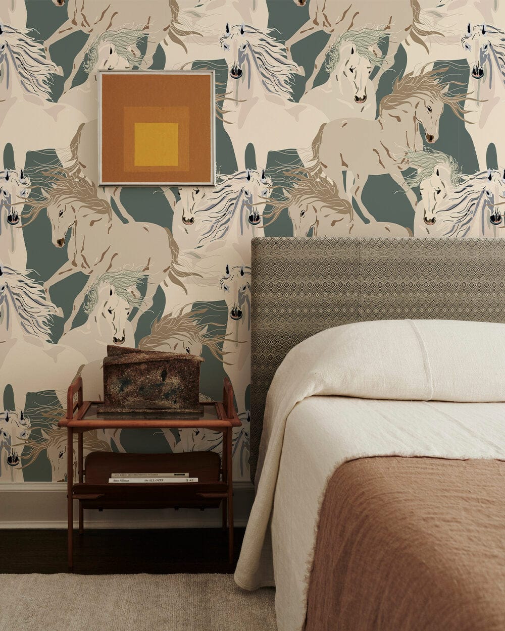Elegant cream and sage horse-patterned mural wallpaper in bedroom with patterned headboard and wooden nightstand.
