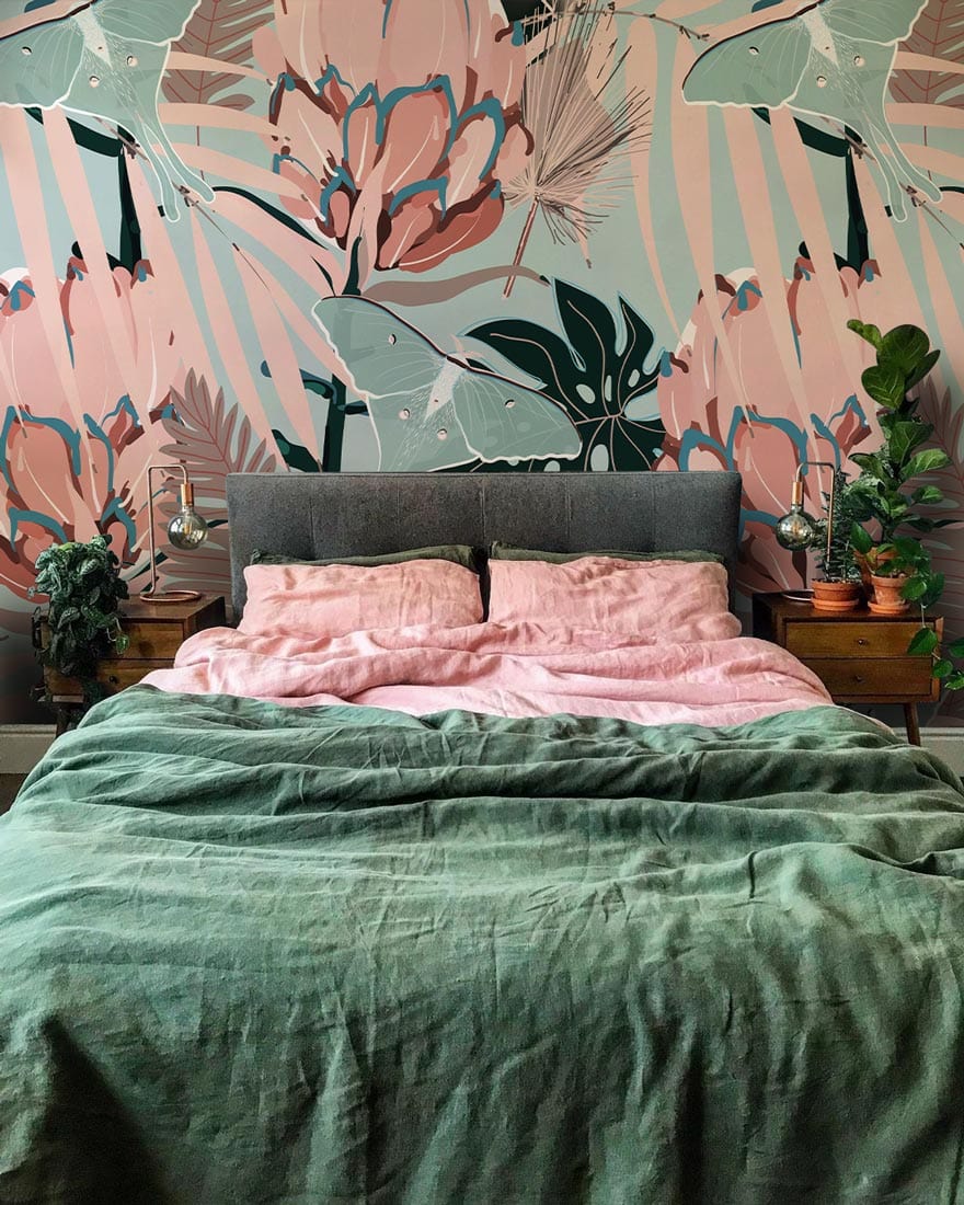 Vintage tropical floral wallpaper with grey headboard, pink duvet, green throw in stylish bedroom.