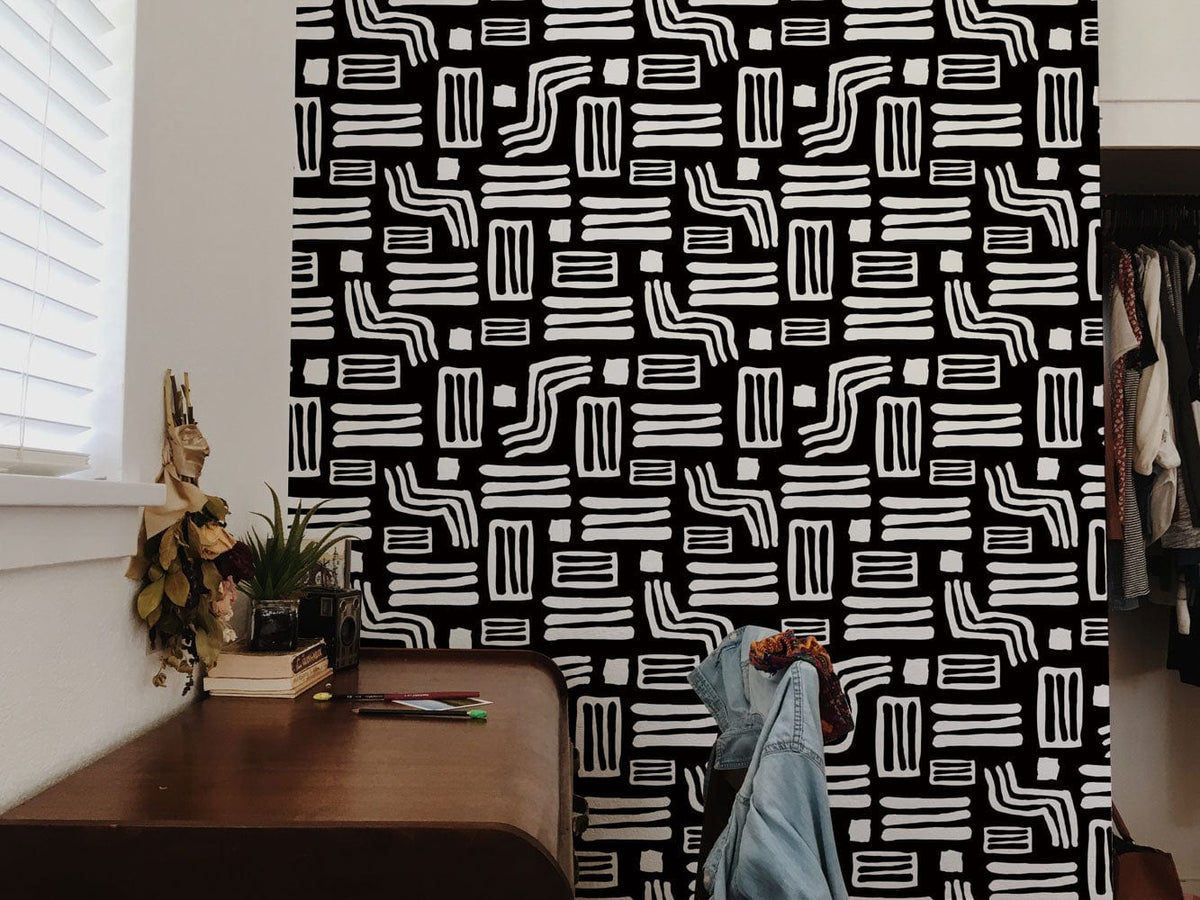 Monochrome geometric tribal wallpaper in room with wooden desk, chair, and casual clothing backdrop.