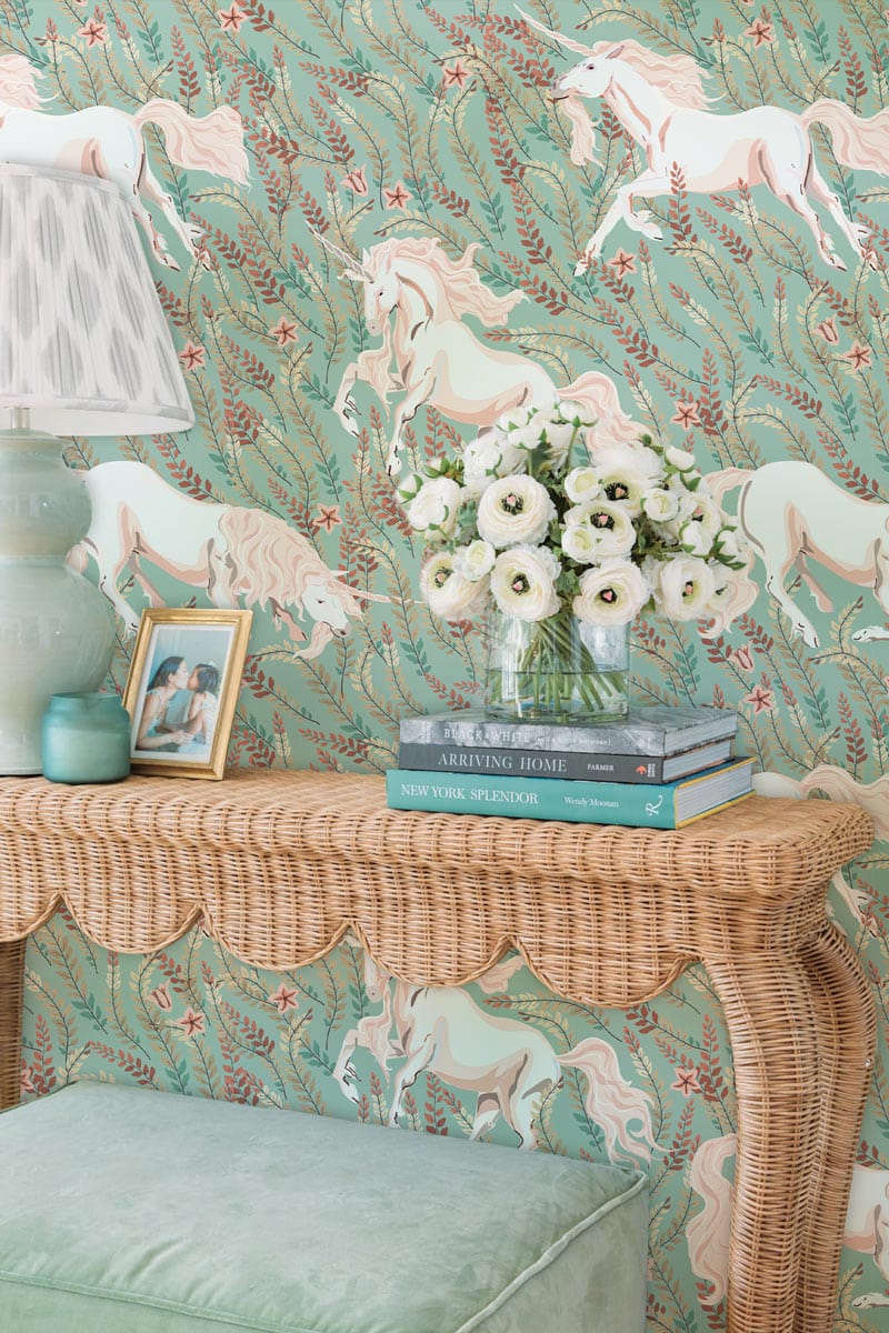 Elegant Unicorn Green Wallpaper; wicker console table, mint velvet stool, soft lighting creating whimsical atmosphere.