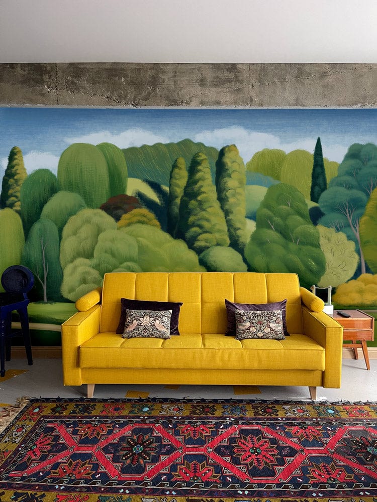 Lush Green Dreamscape mural in living room with yellow sofa, colourful rug, and concrete wall.