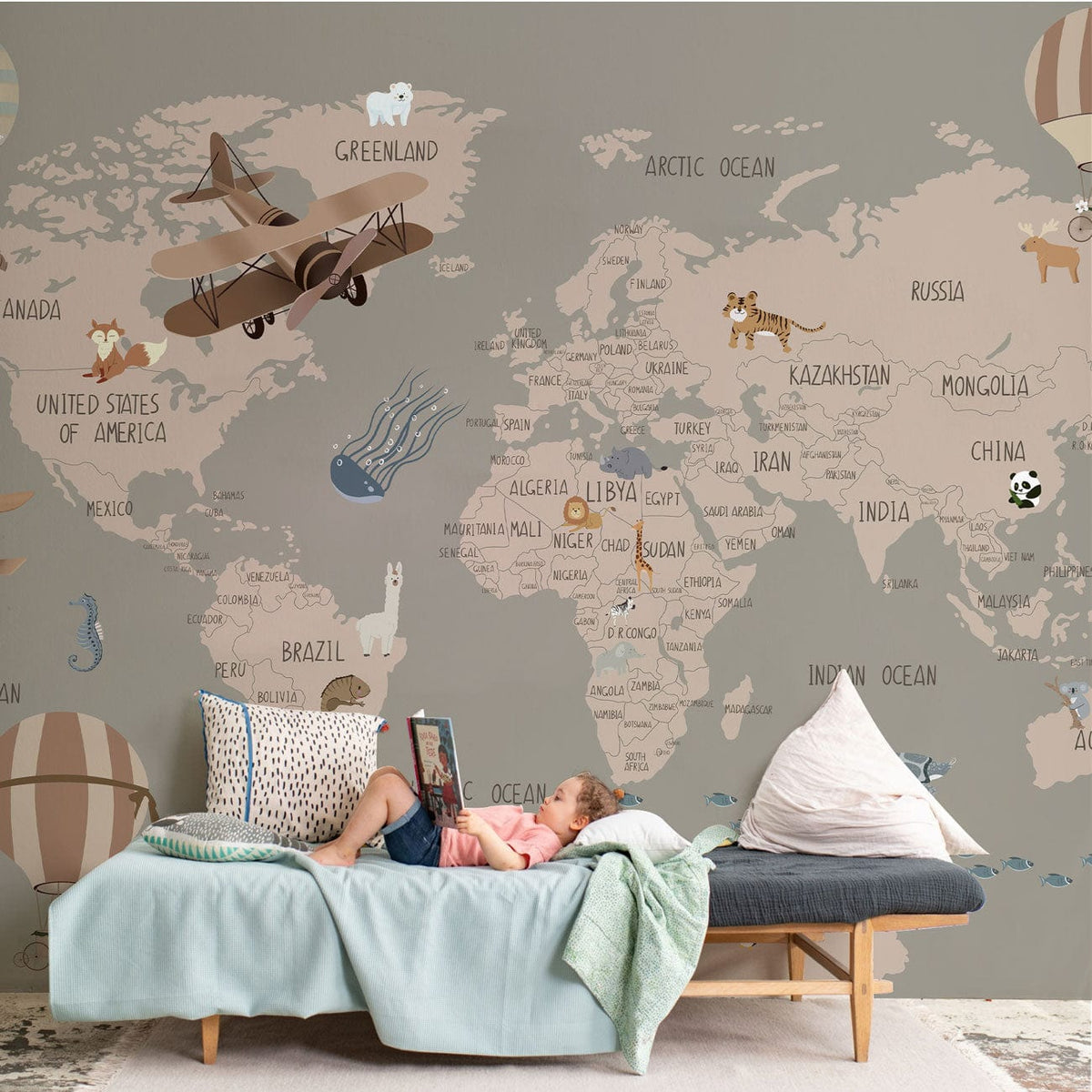 Vintage world map mural wallpaper, taupe tones, featuring aeroplanes, animals, sofa, and decorative cushions.