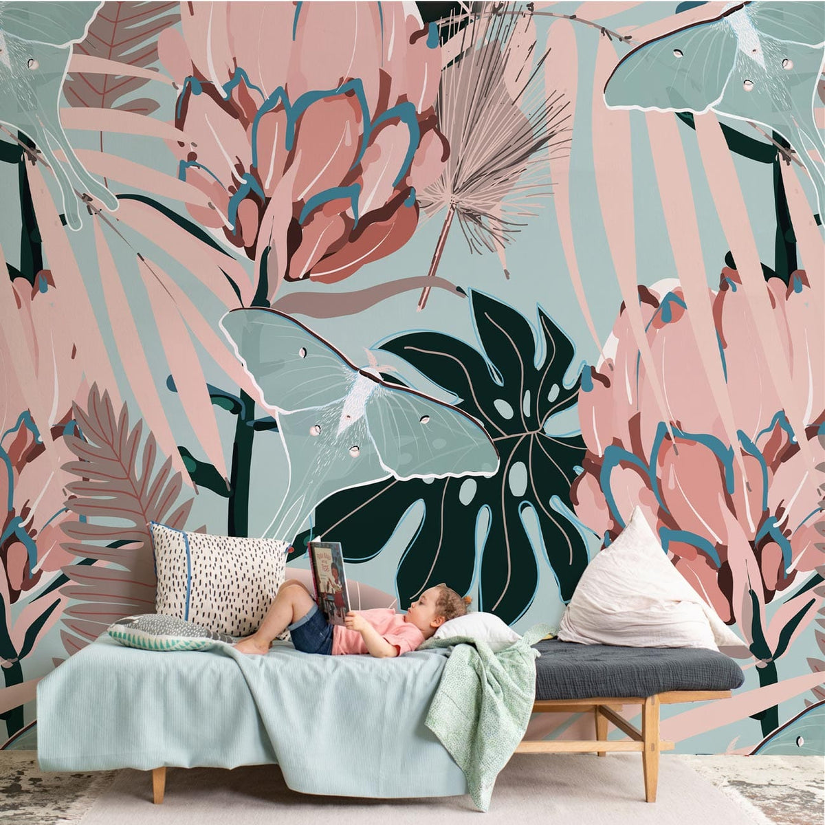 Vintage tropical floral wallpaper in soft pink and teal; girl on sofa with cushions, cosy room.