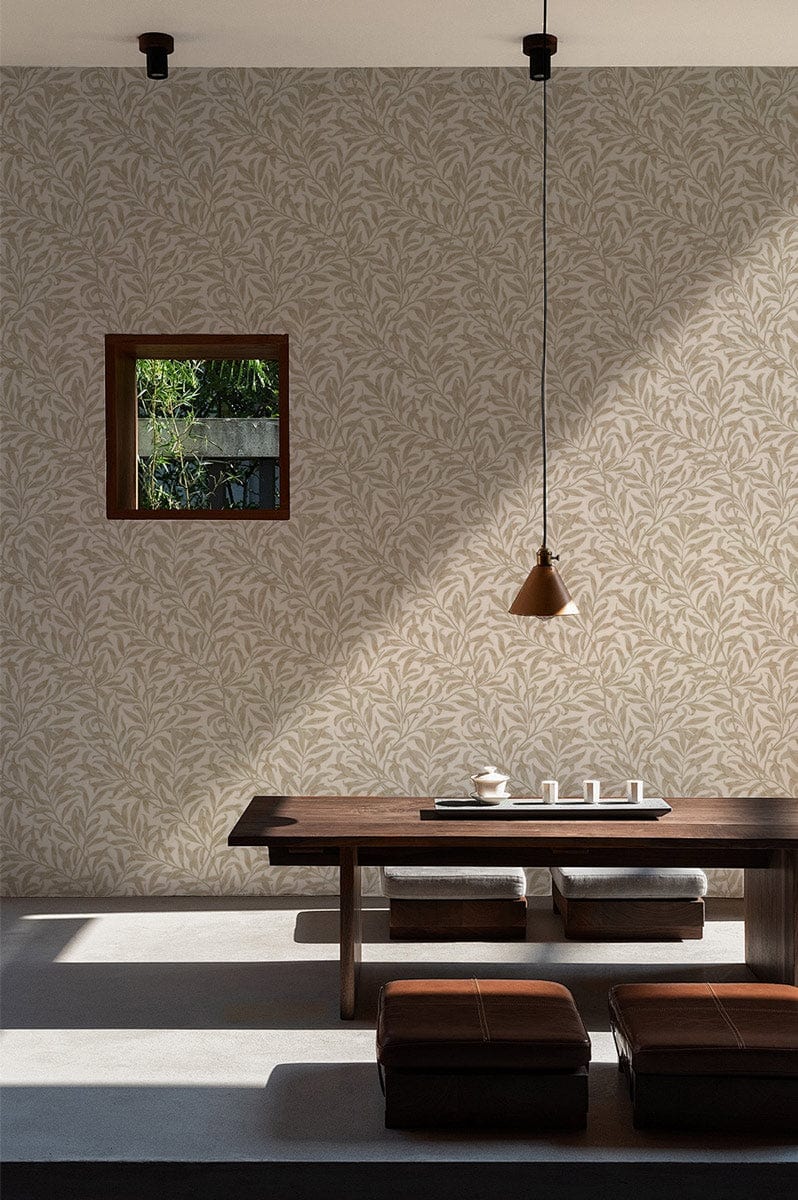 Elegant cream botanical leaf wallpaper in dining room with wooden table, cushions, pendant light, window.