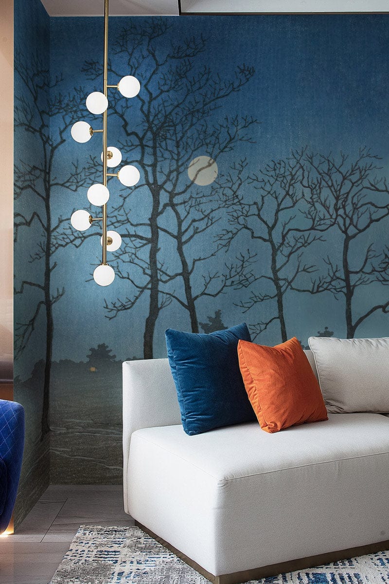 Midnight Mist Blue Woodland Wallpaper in lounge with modern white sofa, colourful cushions, elegant lighting.
