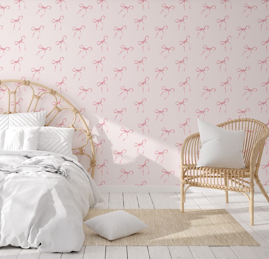 Charming pink bow wallpaper with soft cream background, white bedding, rattan chair, wooden flooring.