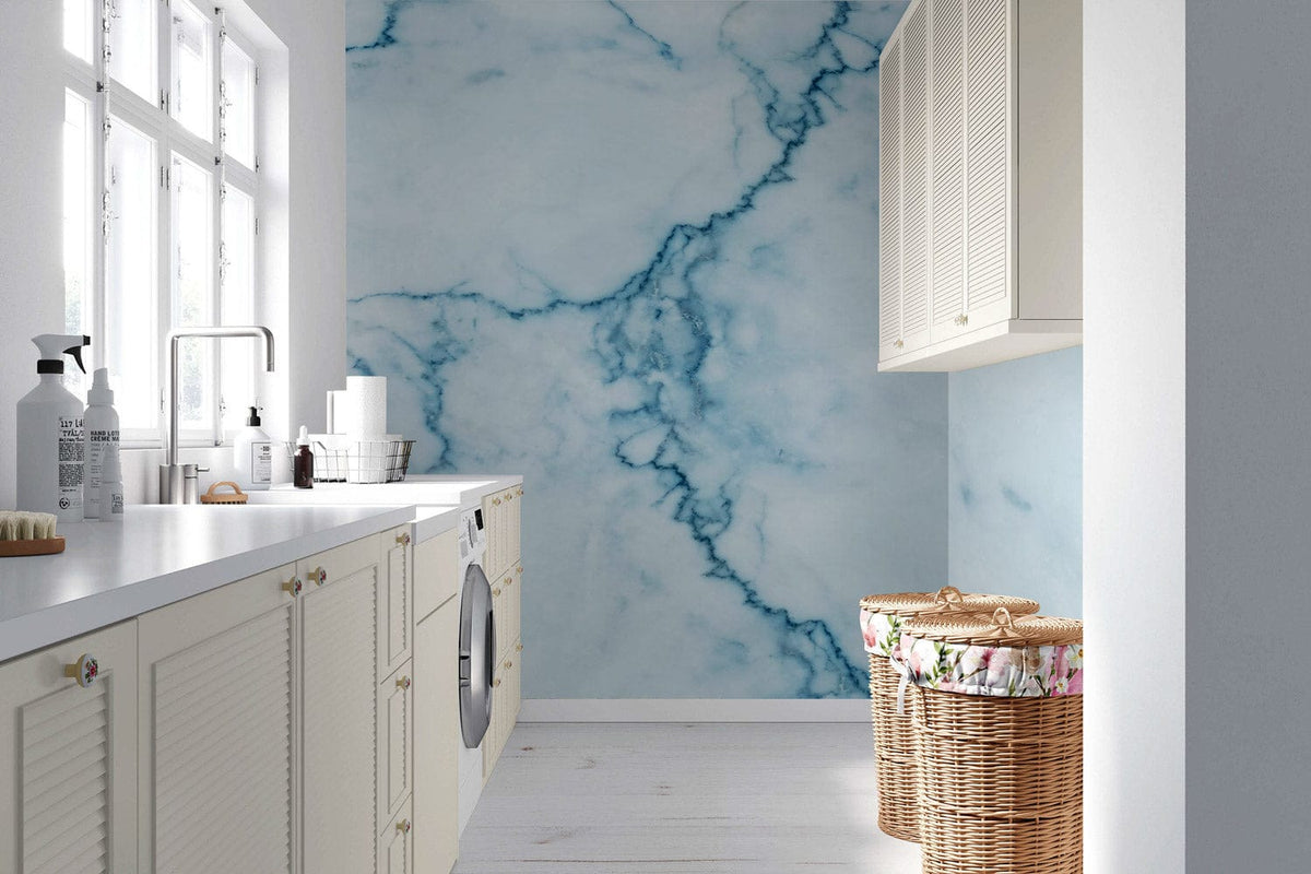 Elegant blue marble wallpaper enhancing modern laundry room, white cabinets, light wood flooring, woven baskets.
