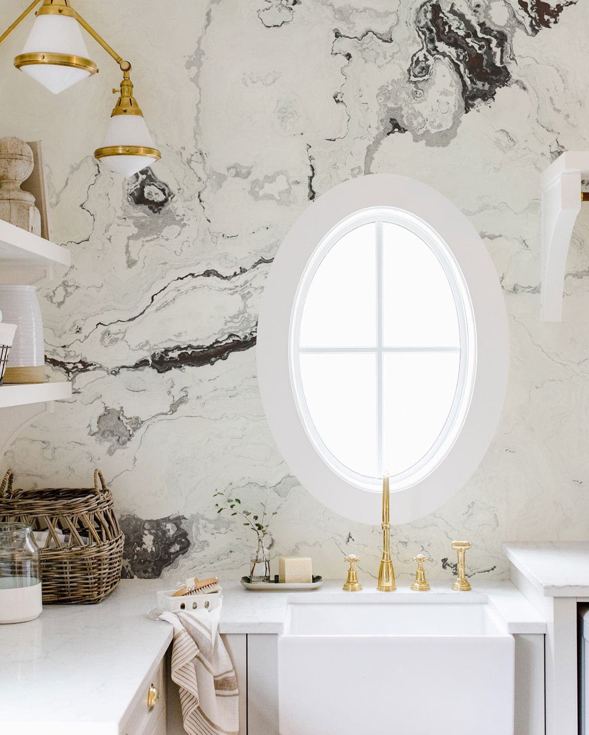 Elegant white marble effect textured wallpaper in kitchen with gold fixtures and farmhouse sink, oval window.