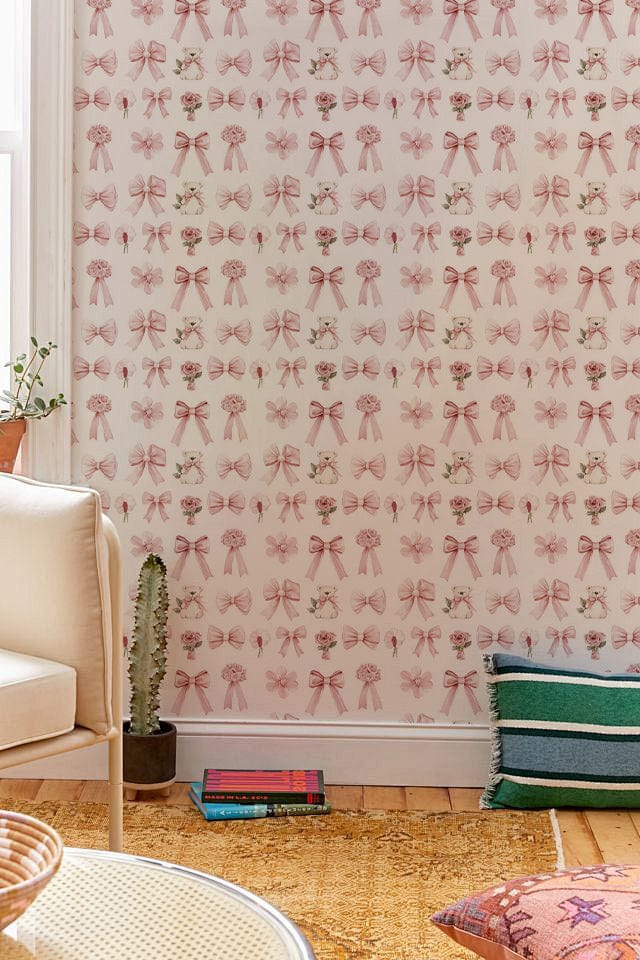 Delicate pink floral vintage wallpaper, beige sofa, wooden flooring, green striped cushion, cosy living room.
