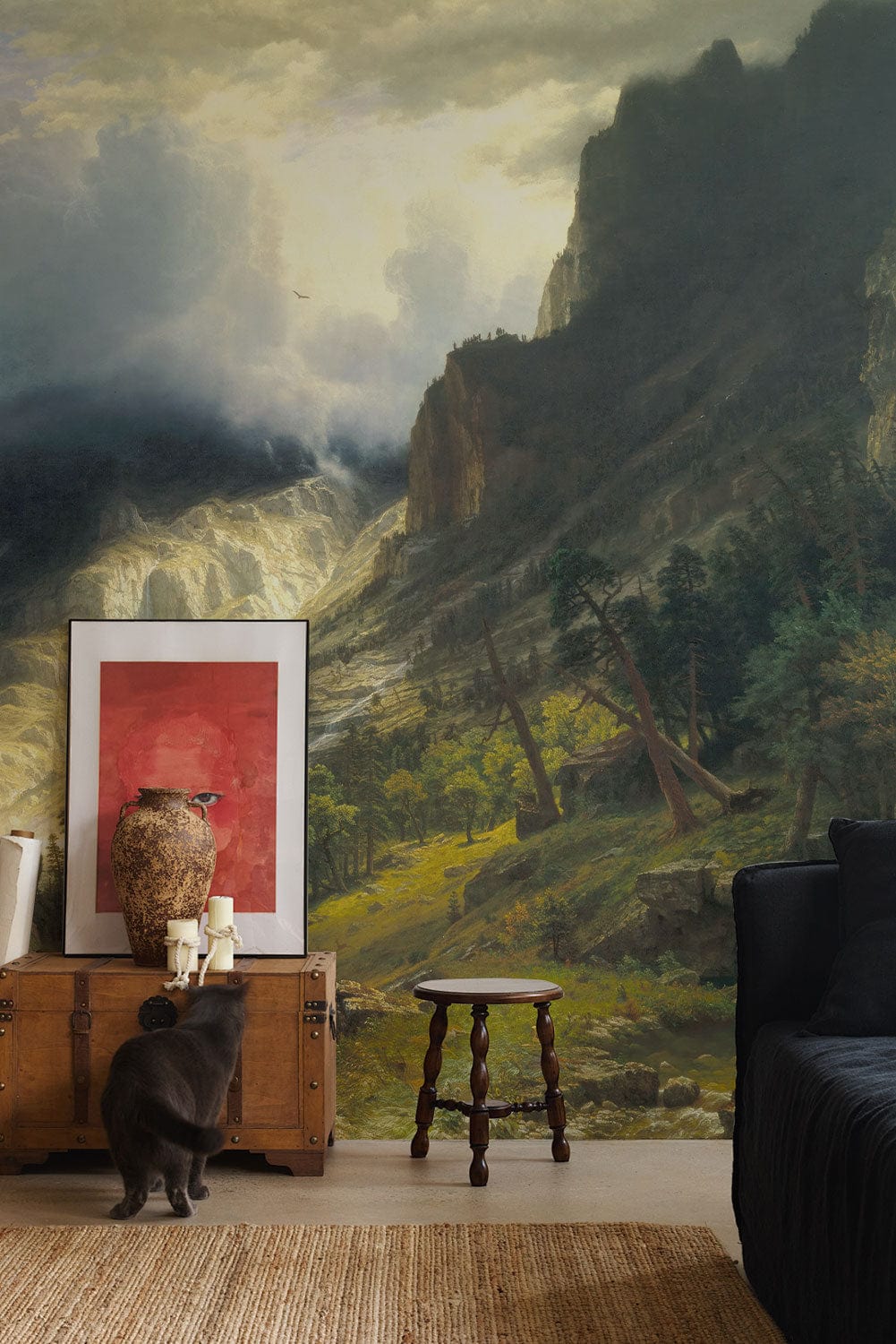 Scenic mountain mural in living room, vintage trunk, black sofa, rustic stool, textured rug flooring.