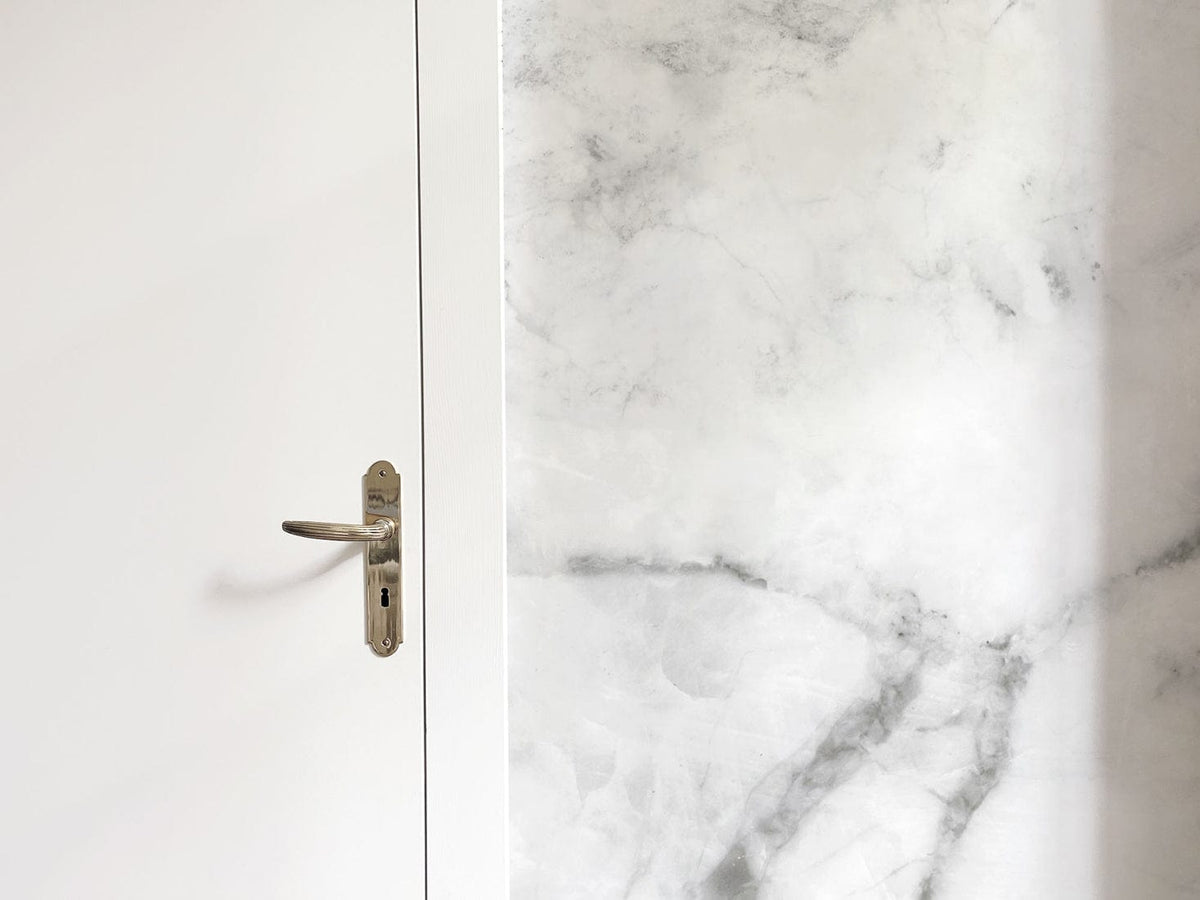 Elegant white marble effect wallpaper in modern interior with white door and silver handle detail.