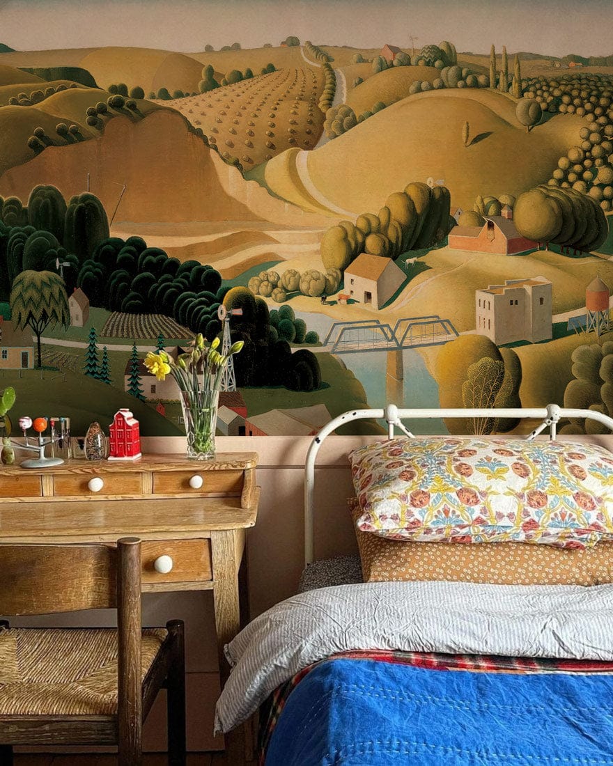 Idyllic Countryside mural wallpaper, earthy tones; rustic bedroom, wicker chair, wooden furniture, colourful bedding.