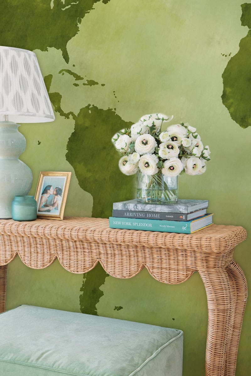 Vintage green world map wallpaper in living room with wicker console, pastel lamp, and mint ottoman.