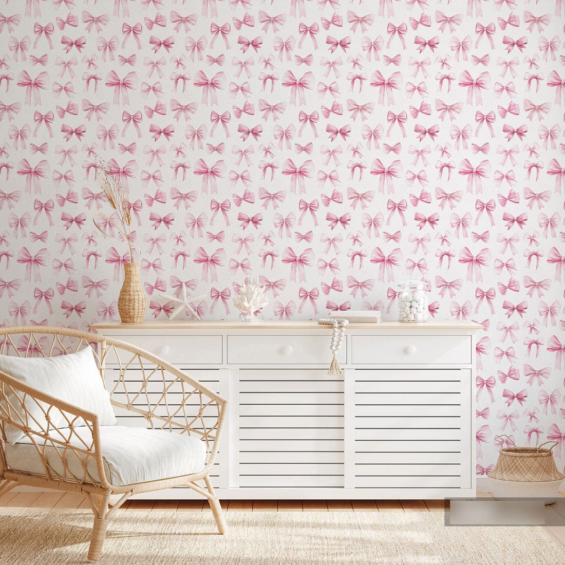 Charming pink bow pattern wallpaper in nursery with white dresser, wicker chair, and light wood flooring.