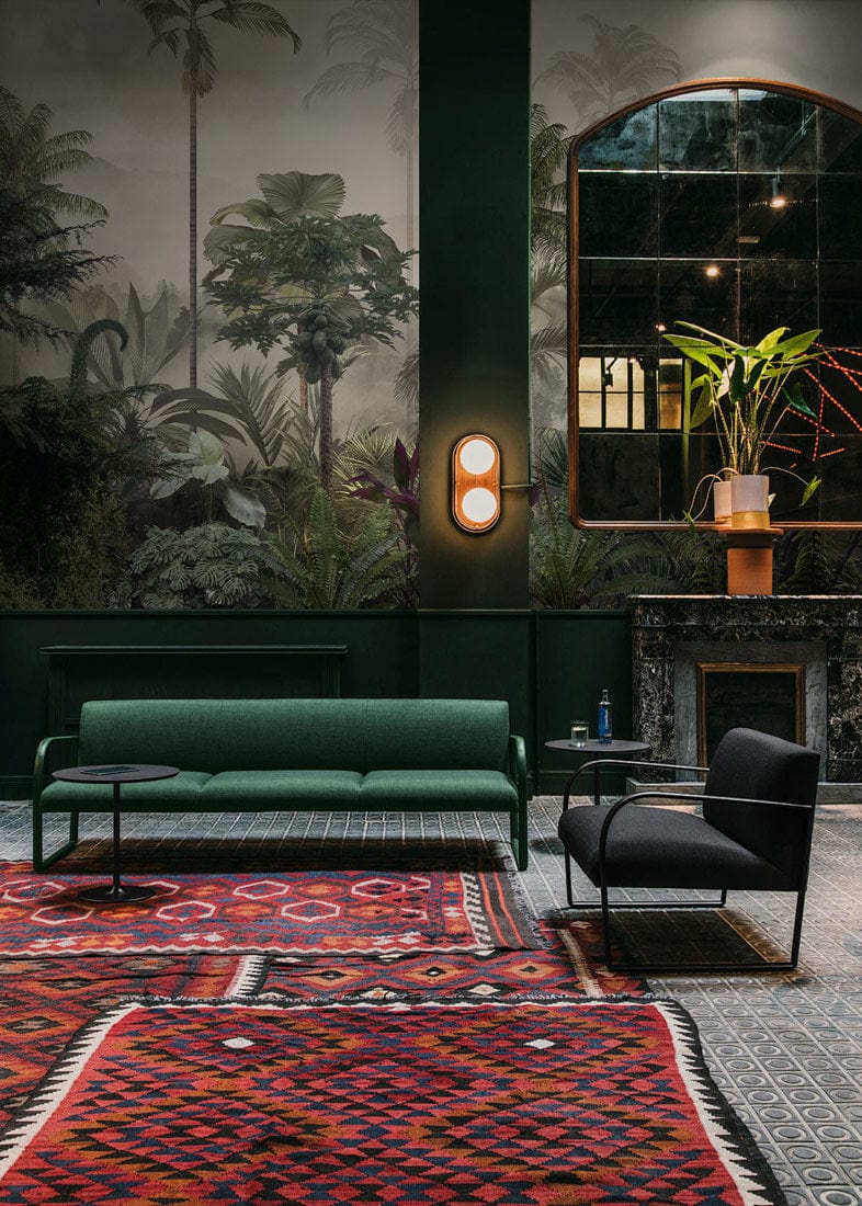 Exotic Tropical Jungle Mural Wallpaper in living room with green sofa, patterned rug, and tiled flooring.