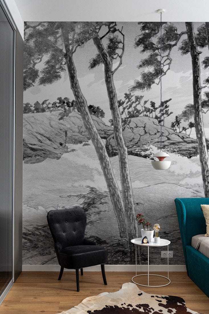 Monochrome coastal forest mural with grey tones, black chair, teal sofa, wooden floor, pendant lighting.