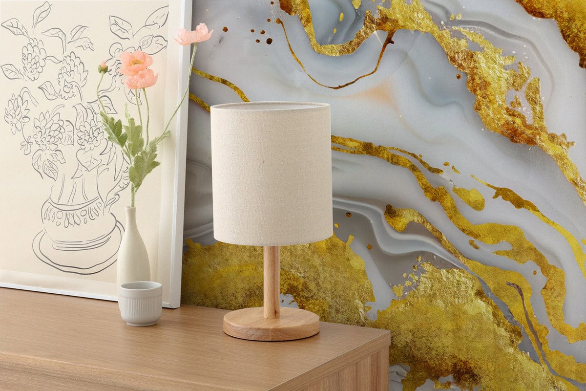 Luxurious gold and white abstract art mural behind wooden table with lamp, flower sketch decor.