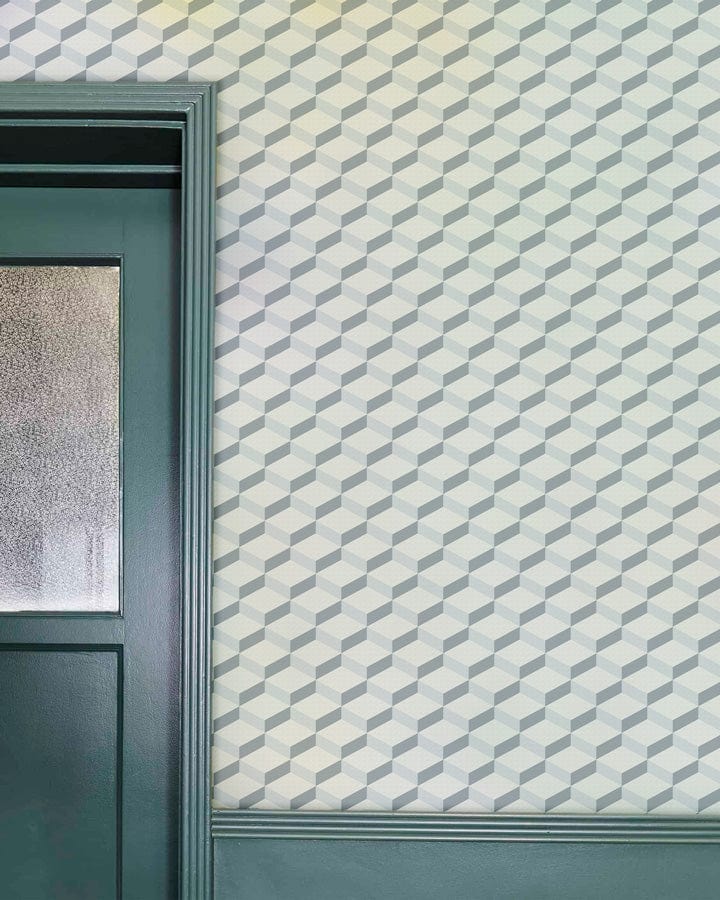 Modern geometric grey and white patterned wallpaper with green door in elegant interior space.