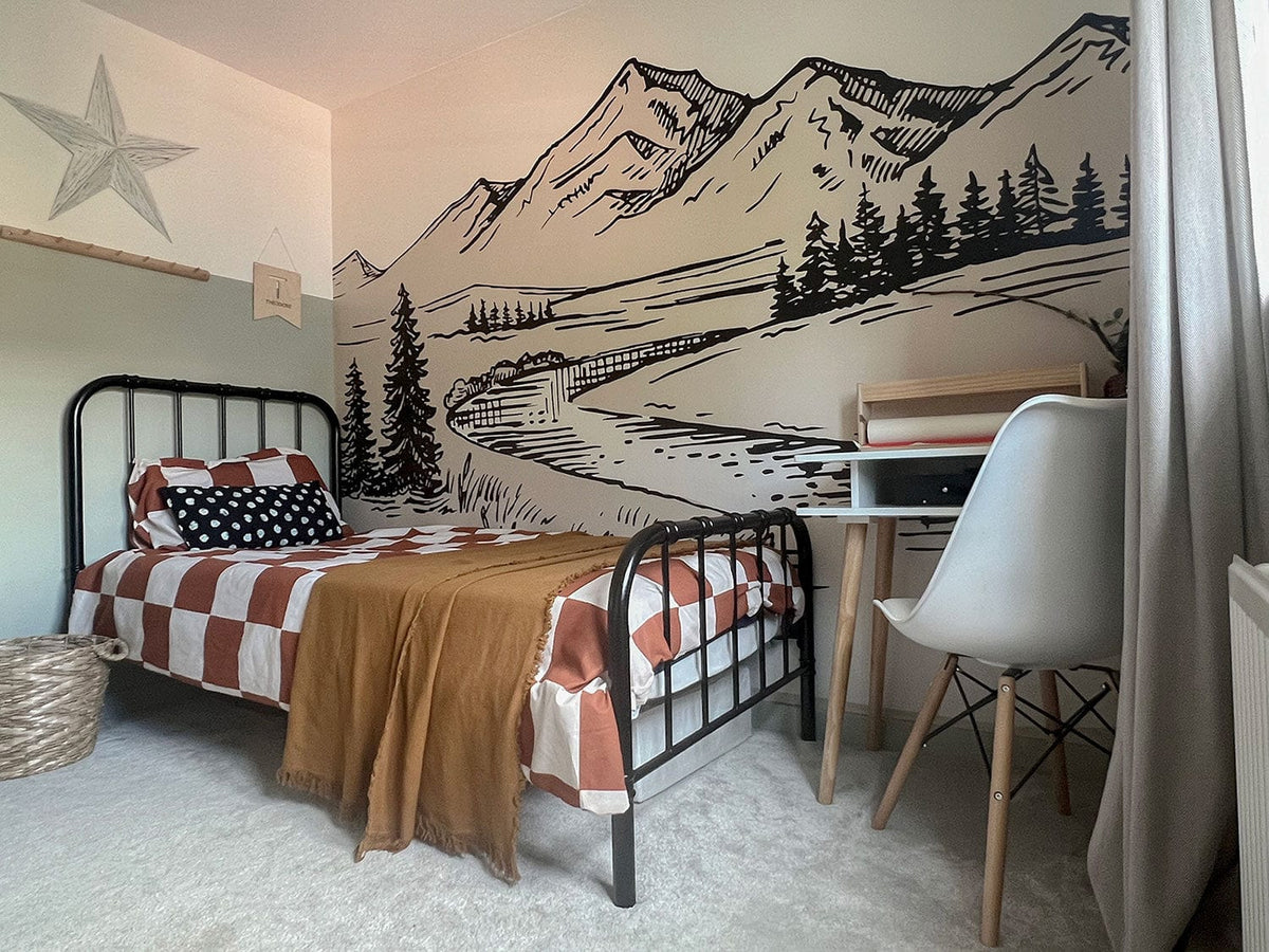 Children's room with Tranquil Mountain Scene mural wallpaper, metal bed, checked bedding, wooden desk.