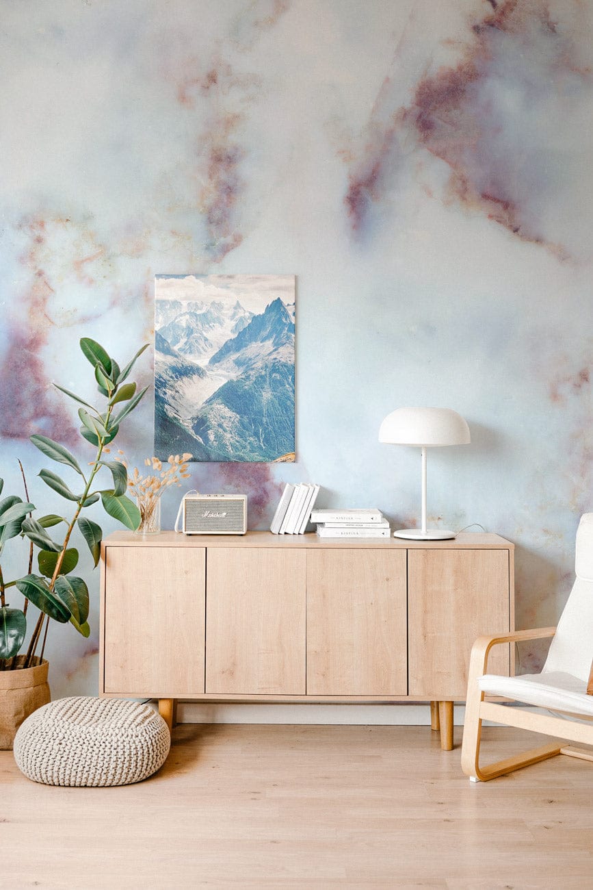 Abstract watercolour mural wallpaper, wooden sideboard, white chair, lamp, plant, light wood flooring, cosy room.