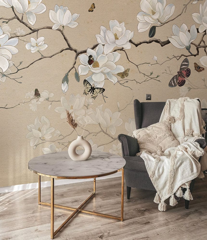 Beige magnolia and butterfly floral mural with grey armchair, golden coffee table, wooden floor.
