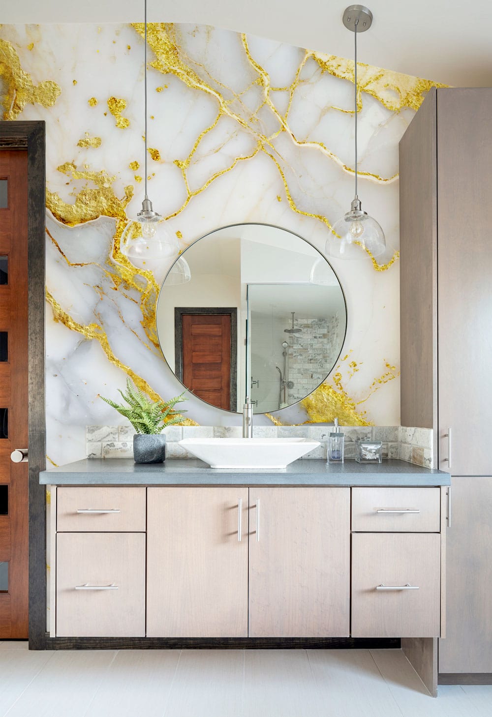 Luxurious gold-veined marble wallpaper in bathroom with round mirror, wooden cabinets, and pendant lights.