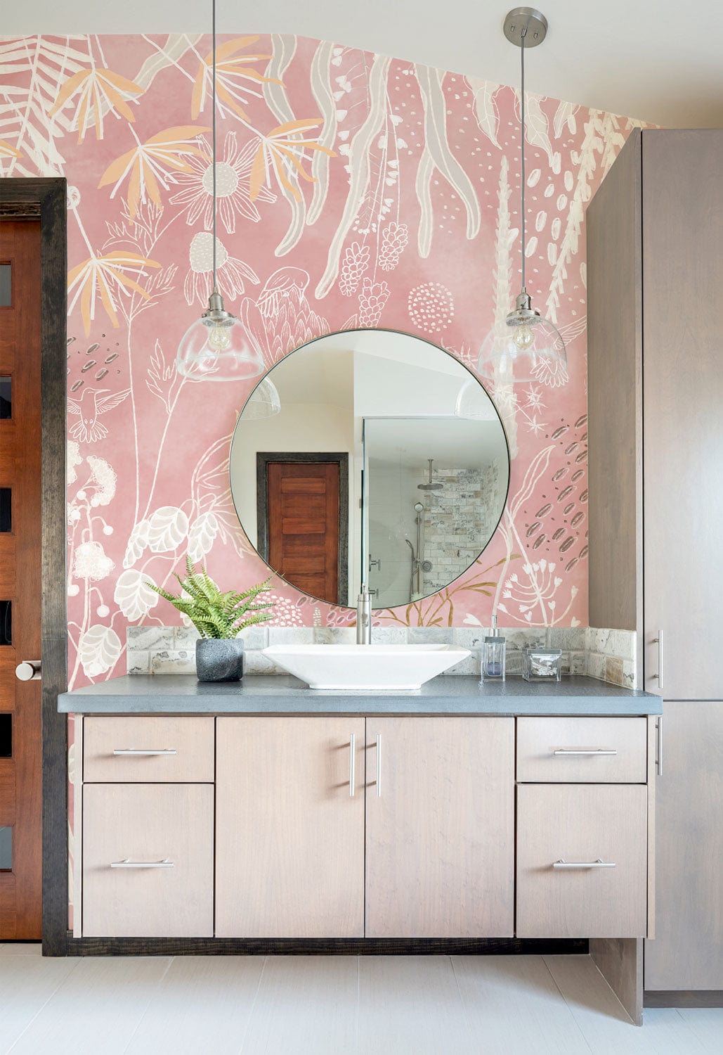 Bathroom with Rustic Blush Botanical Mural Wallpaper, round mirror, light wood vanity, pendant lights.