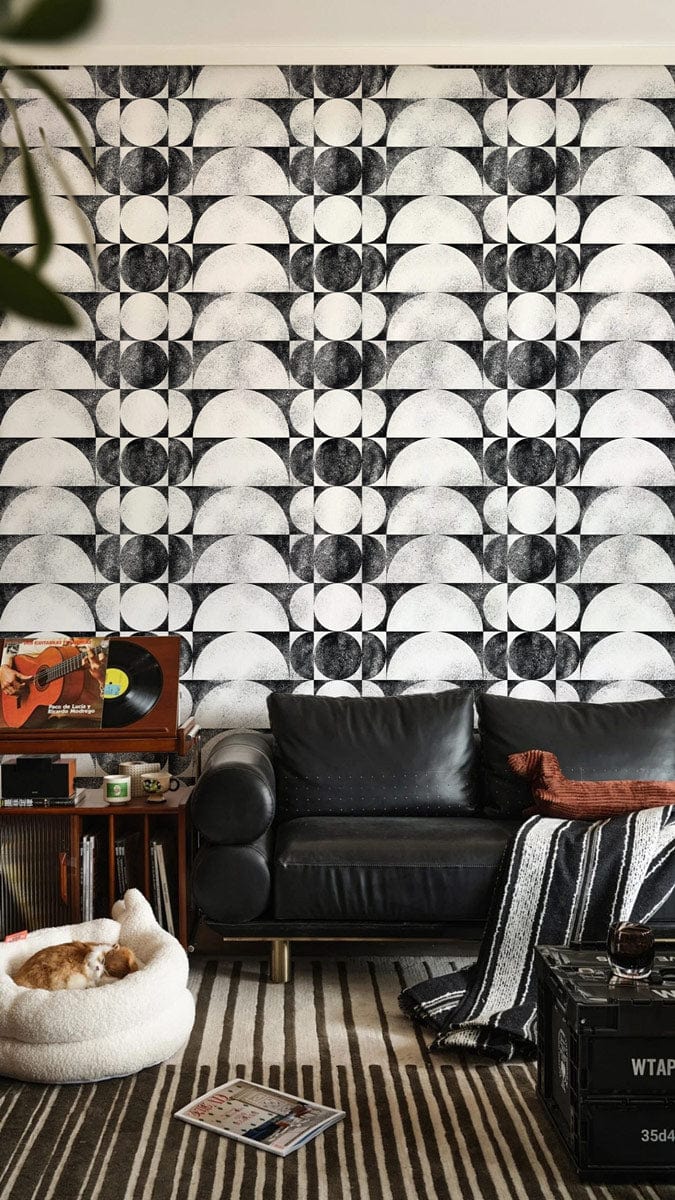 Monochrome geometric wallpaper, black sofa, stripe rug, modern room, cosy cat bed, record player.