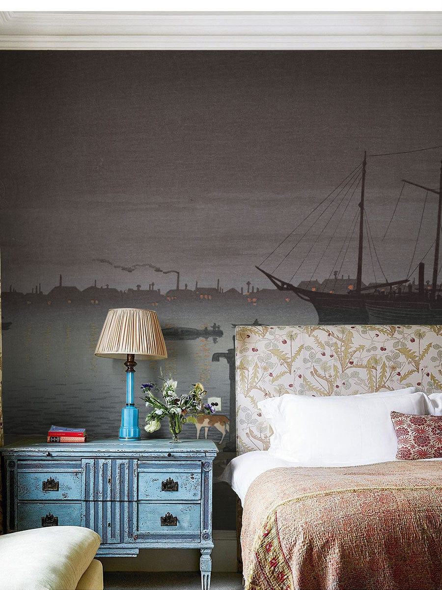 Tranquil Seaside Vintage Mural Wallpaper in bedroom with blue chest, floral headboard, and ambient lighting.