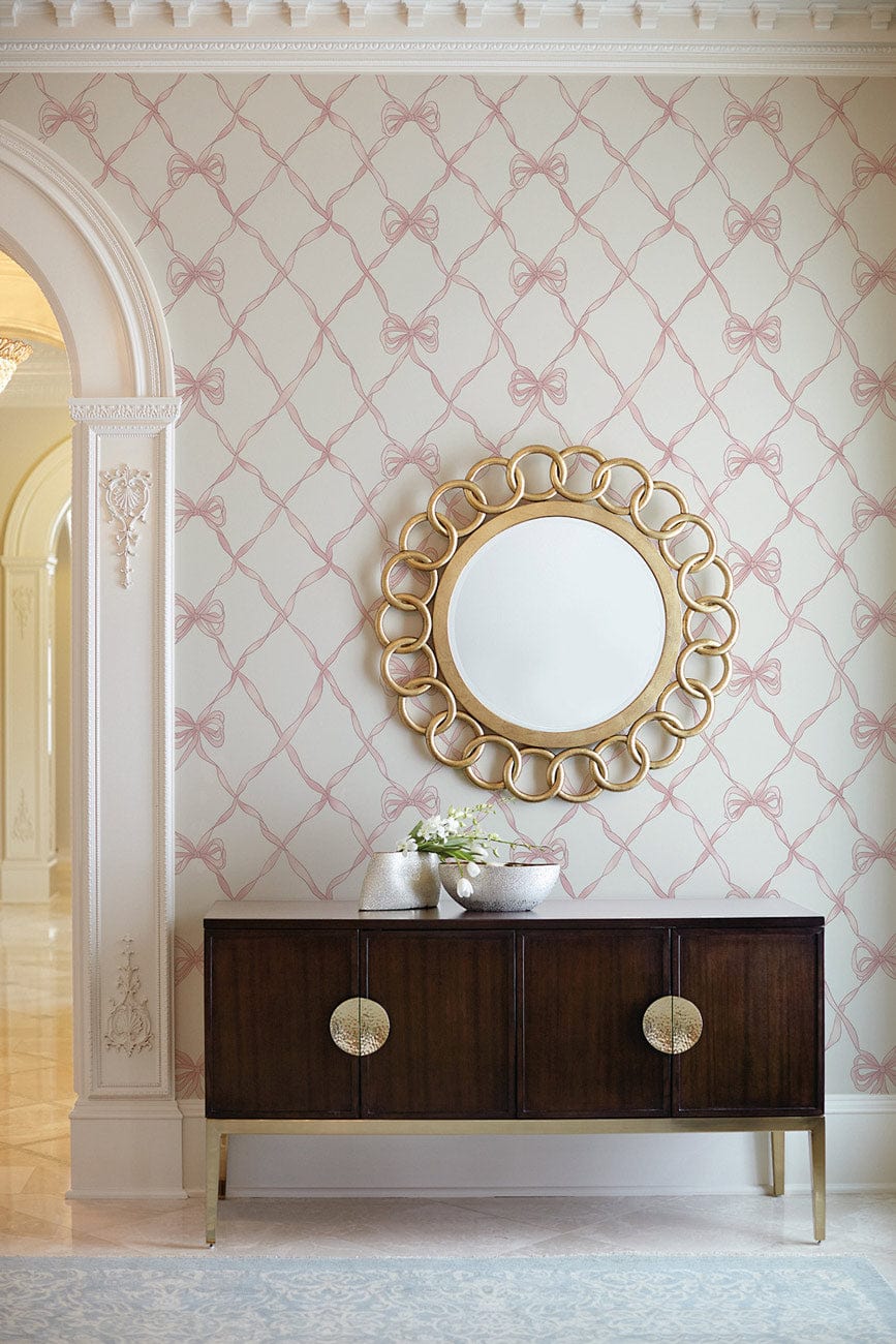 Elegant pink bow wallpaper in classic British style, with gold mirror, dark wooden sideboard.