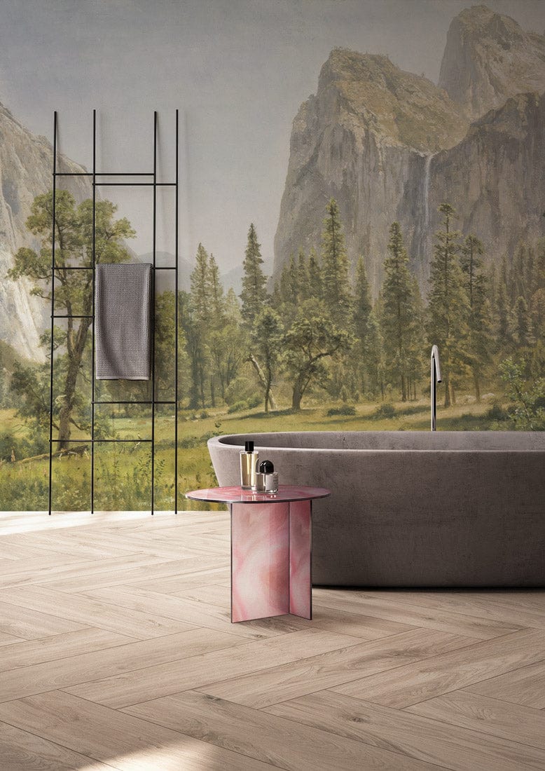 Majestic Mountain Landscape Mural Wallpaper, grey bathtub, pink side table, herringbone wood flooring, towel rack.