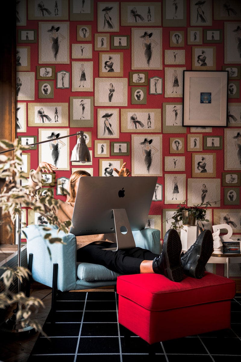 Vintage red-toned wallpaper with framed artwork, blue armchair, black tile floor in stylish room.