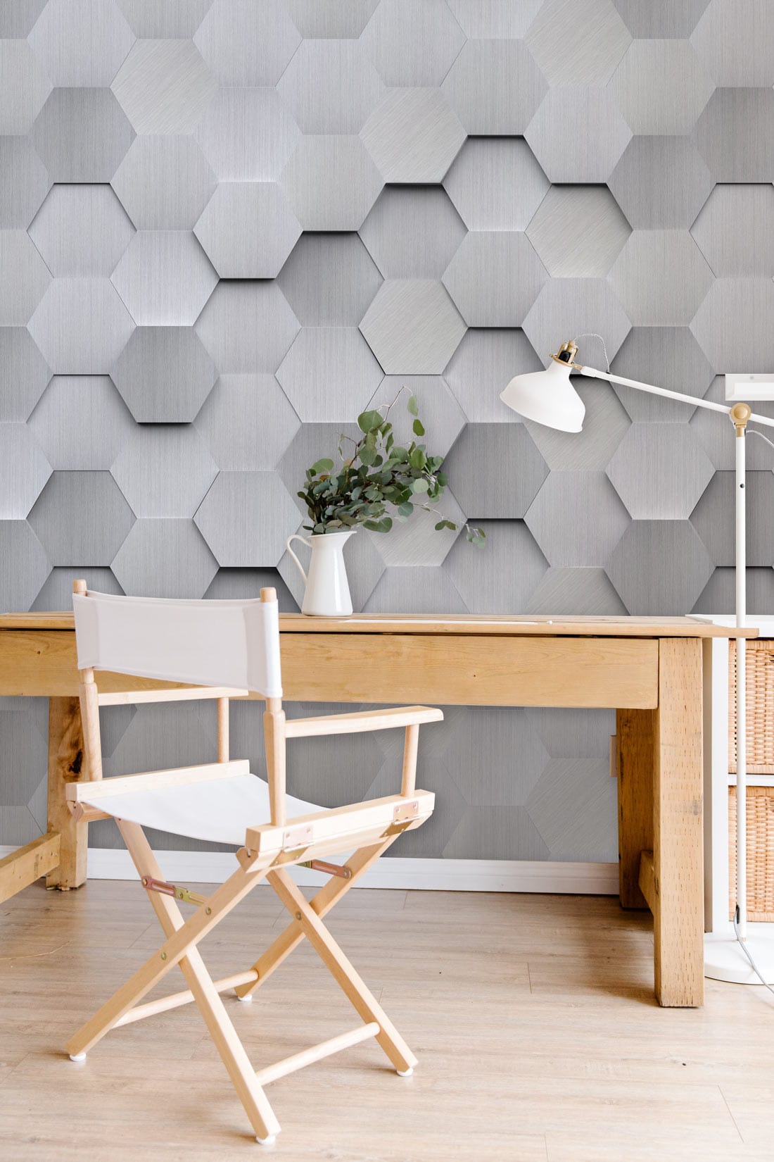 Modern silver hexagonal 3D geometric wallpaper, wooden desk, white chair, lamp in stylish room.