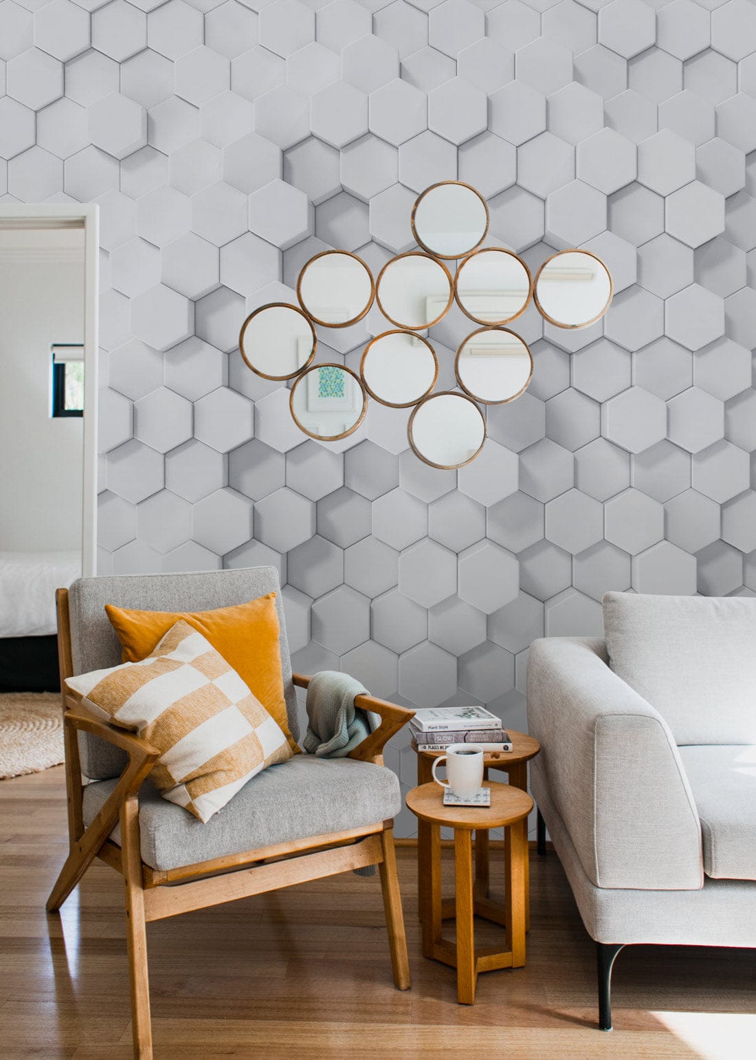 Geometric white hexagonal 3D wallpaper in living room with grey sofa, wooden flooring, and mirrors.