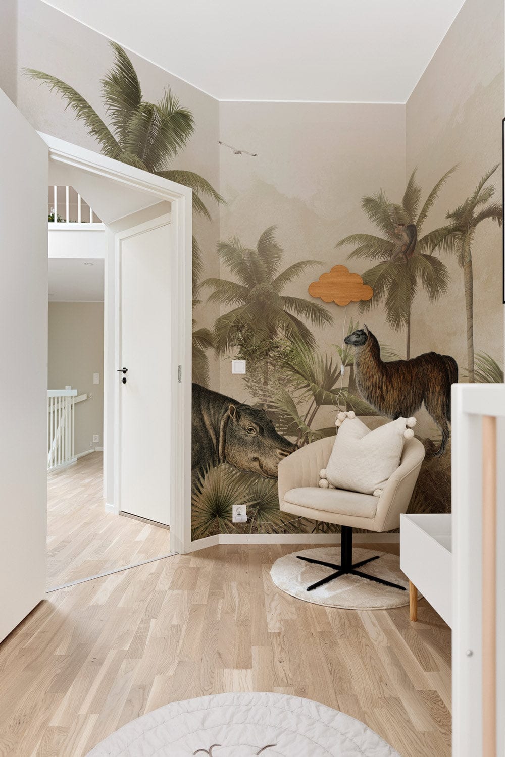 Vintage Jungle Safari Mural Wallpaper with animals; beige armchair; wood flooring; modern nursery design.