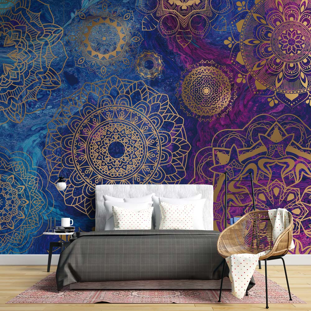 Elegant mandala wallpaper in gold, blue, and purple; grey bed, patterned chair, wooden floor, bedroom.