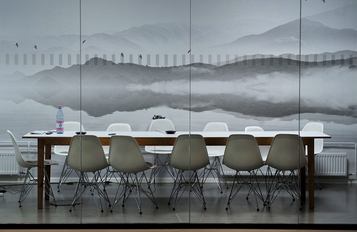 Tranquil Misty Mountains mural in conference room with white chairs, wooden table, grey flooring.