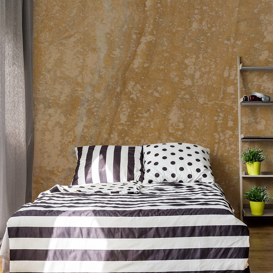 Golden Earth rustic yellow stone wallpaper behind a striped black and white bed in a cosy bedroom.