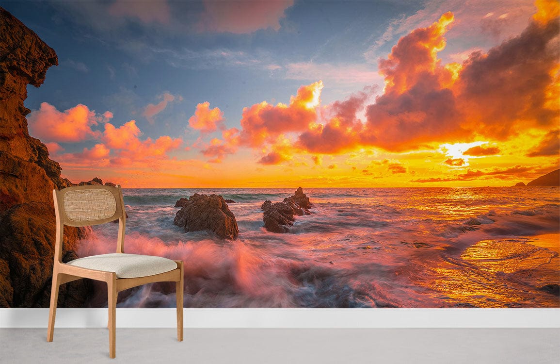 Vibrant sunset seascape mural wallpaper with wooden chair; dramatic coastal colours, waves in lounge setting.