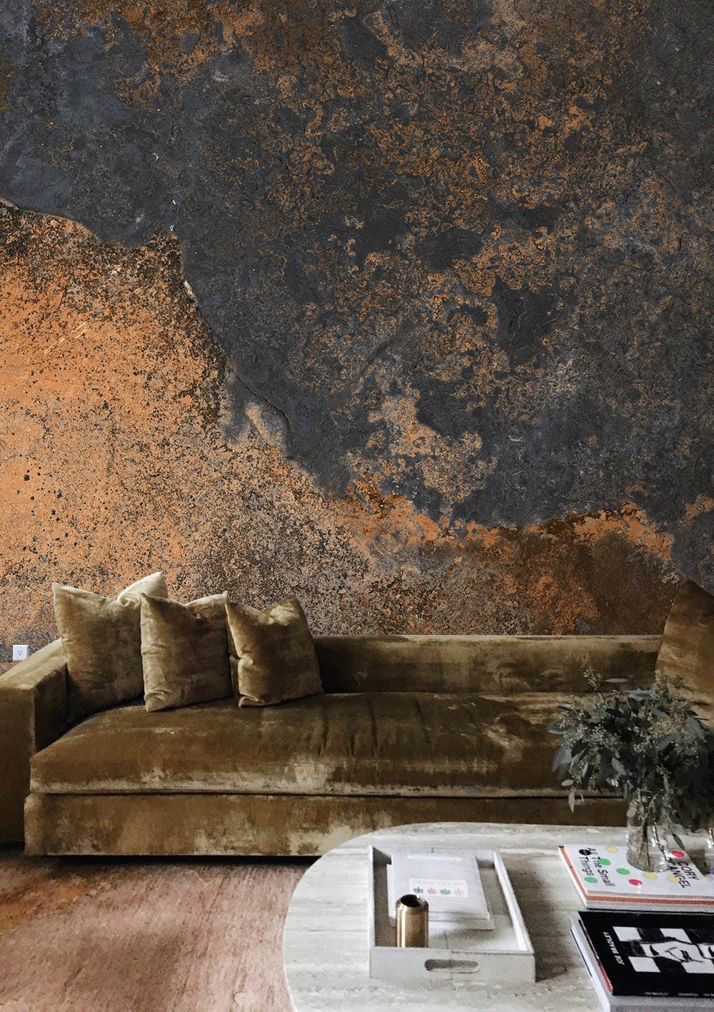 Vintage industrial mural wallpaper with earthy tones, velvet sofa, rustic flooring, and round table.